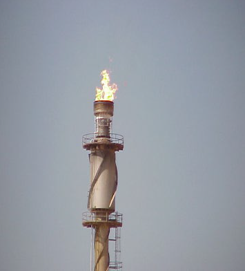 Flare stack with a small clean flame after HP Air Assist installation, seen against a clear sky
