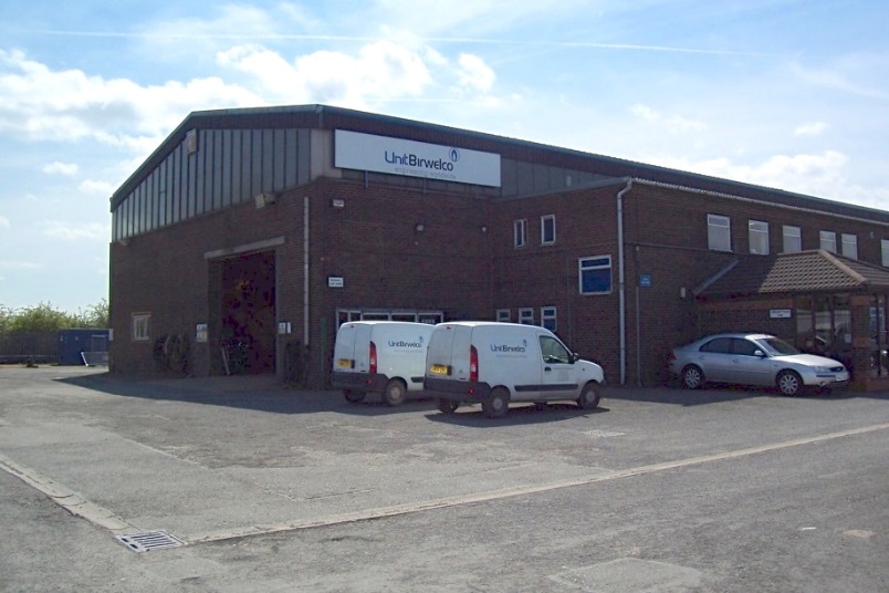 UnitBirwelco manufacturing facility — brick building with branded company vans parked outside